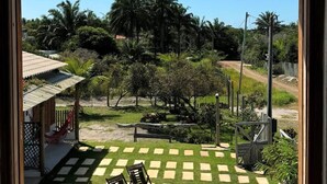 A view from a window of a backyard with a checkered lawn, a pool, and surrounding greenery. - Casa Mangaba da Praia (Prado)