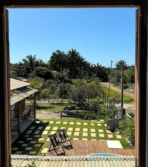 Vista desde una ventana de un jardín trasero con césped a cuadros, una piscina y abundante vegetación.