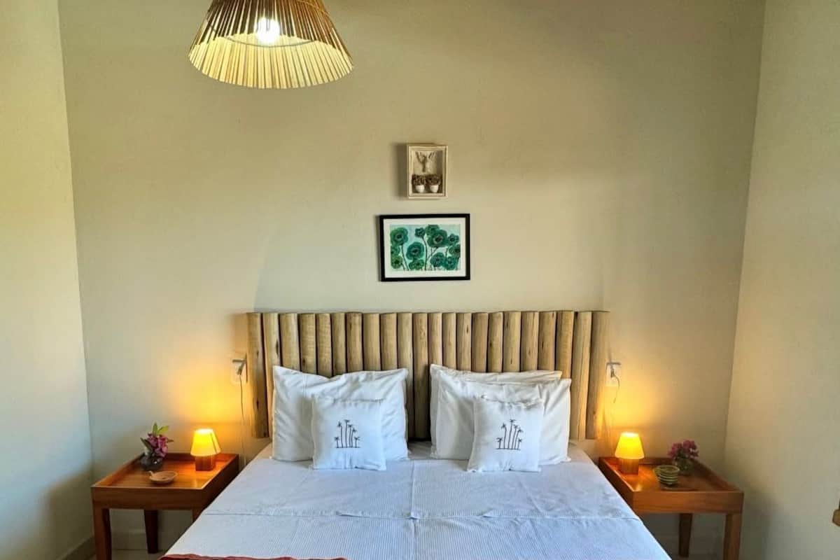 A double bed with a striped bedspread, two bedside tables with lamps, a wooden headboard, a wall-mounted picture, and a hanging light fixture.
