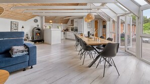 Ett modernt kök med en central köksö, en matplats med ett långt bord och stolar samt en mysig sittgrupp med en soffa.