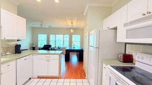 Een moderne keuken met witte kasten, een centraal eiland, een eethoek met een zwarte tafel en uitzicht op de omgeving door grote ramen.