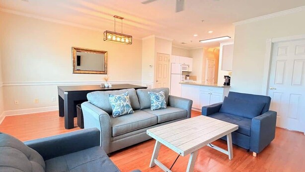 Een woonkamer met een bank, een salontafel en een eettafel met stoelen. Achtergrond is een keuken.