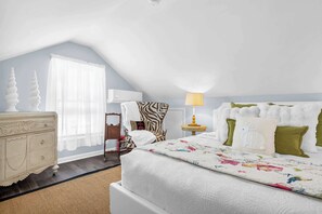 Ein Schlafzimmer mit Bett, Kommode, Lampe und einem Fenster mit Vorhängen.