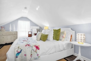 A bedroom with a bed, pillows, a bedside table, a dresser, and a window.