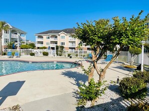 Ein Swimmingpool mit weißem Zaun, Liegestühlen und einem Gebäude mit Balkonen im Hintergrund.