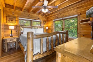Ein Schlafzimmer einer Holzhütte mit einem Bett, zwei Nachttischen, einem Deckenventilator und großen Fenstern.