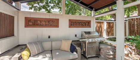 Une terrasse extérieure dotée d’un barbecue intégré et d’un espace salon confortable avec des coussins.