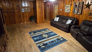 Een kamer met houten wanden, een plafondventilator, een bruine leren bank, een kamerbreed tapijt en een houten vloer.
