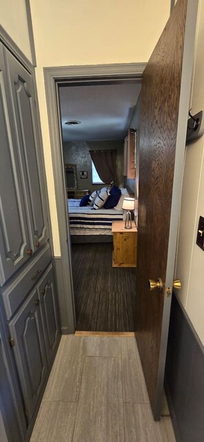Ein schmaler Flur führt zu einem Schlafzimmer mit einem Bett, einem Nachttisch und einem Fenster.