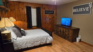 Een slaapkamer met een bed, een dressoir, een televisie en een inspirerende leus.