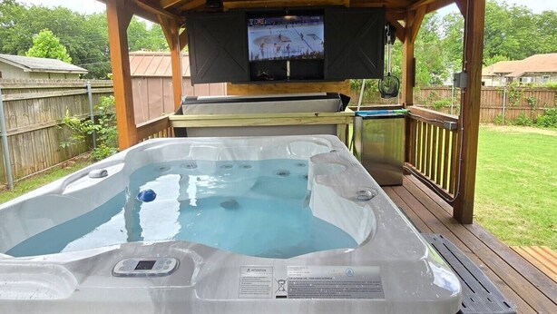 Een hottub met erboven een televisiescherm, omringd door een houten terras en een houten schutting.