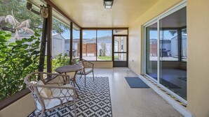 Ein überdachter Balkon mit Korbmöbeln, einem gemusterten Teppich und Blick auf den Garten.