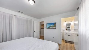 Ein Schlafzimmer mit Bett, einem Gemälde, einem Badezimmer mit Waschbecken und Spiegel sowie einem Flur, der zu einem weiteren Raum führt.