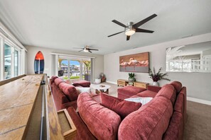 Sala de estar com mesa de bilhar, sofás vermelhos, ventiladores de teto e uma grande janela com vista.