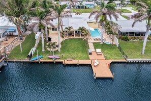 A residential property with a swimming pool, palm trees, and a dock extending into a body of water. - 3BR Waterfront Home with Pool & Kayaks (Cocoa Beach)