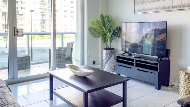 Un salon moderne avec un téléviseur à écran plat, une table basse, une plante en pot et un canapé.