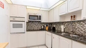 Une cuisine moderne avec des meubles blancs, un four à micro-ondes, un four traditionnel, un pare-feu en carrelage et un évier en acier inoxydable.