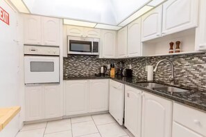 Cozinha moderna com armários brancos, micro-ondas, forno, painel de azulejos e pia de aço inoxidável.