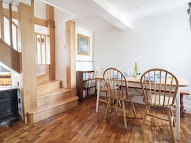 Un comedor con sillas y una mesa de madera, una escalera con barandillas de madera y una estantería llena de libros.