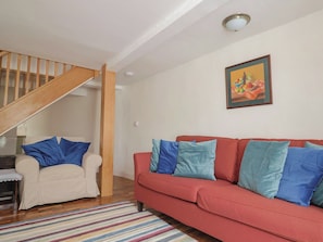 Una sala de estar con una escalera, un sofá rojo, un sillón blanco y un tapete colorido a rayas.