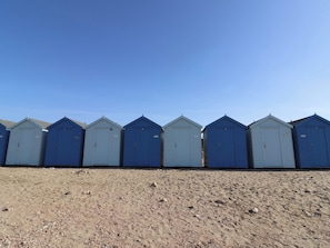 A row of beach huts with a sandy foreground. - Saybrook Cottage (Bridport)