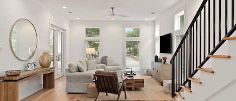 A spacious living area with a sofa, a chair, a wooden coffee table, and a TV mounted on the wall.