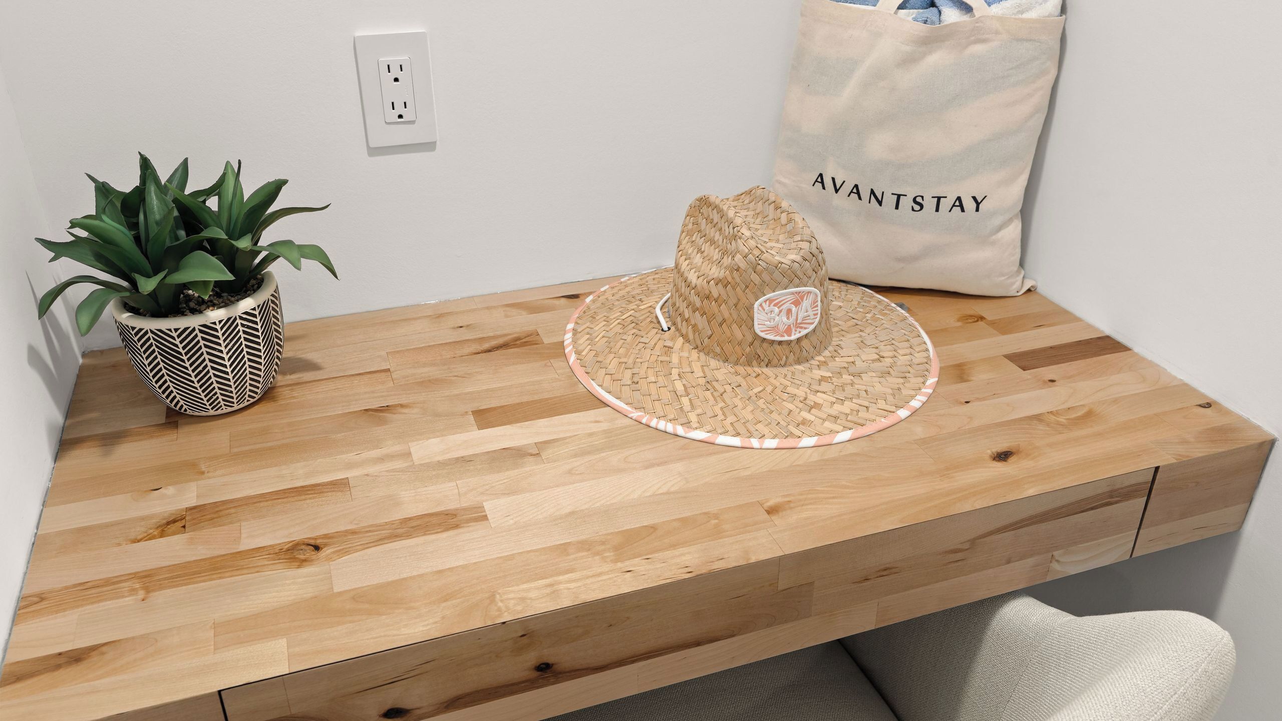 A wooden desk with a woven hat, a potted plant, and a tote bag labeled 'AVANTSTAY'.