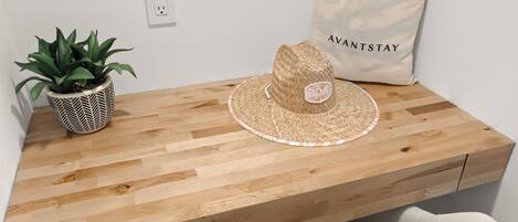 A wooden desk with a woven hat, a potted plant, and a tote bag labeled 'AVANTSTAY'.