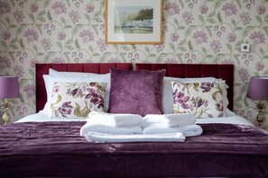 A neatly made bed with floral pillows and a folded towel, a red headboard, and a framed picture on the wall. - Western Isles Hotel (Tobermory)