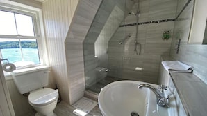 Une salle de bain équipée de toilettes, d’un lavabo, d’une douche et d’une fenêtre donnant sur un paysage agréable.