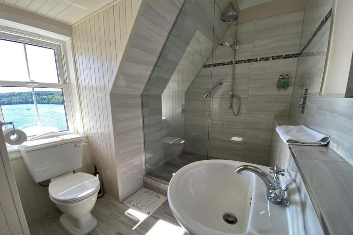 A bathroom with a toilet, a sink, a shower, and a window with a view.