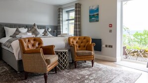 Une chambre à coucher avec un lit, deux fauteuils, une petite table ronde et une vue sur l’extérieur.