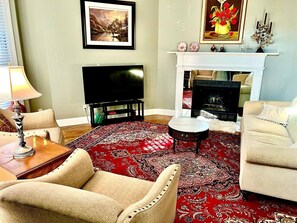 Ein Wohnzimmer mit Fernseher, Kamin und einem roten Teppich mit Muster.