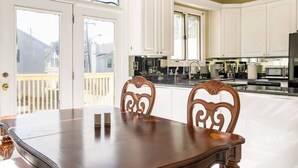 A dining area with a wooden table and chairs, a kitchen with white cabinets, and a view through a glass door. - Forsyth Silk-n-art (elegance-comfort-free parking) (Savannah)