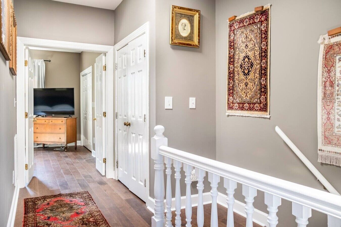 Un couloir avec un téléviseur, une commode en bois, des portes blanches et des tapis à motifs.