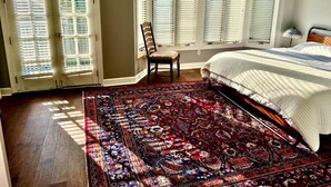 A bedroom with a large bed, a patterned rug, a chair, and a window with blinds. - Forsyth Silk-n-art (elegance-comfort-free parking) (Savannah)