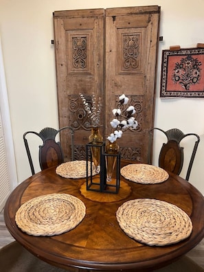 Ein runder Holztisch mit gewebten Tischsets, zwei Vasen mit Baumwollblumen und einer dekorativen Metallablage.