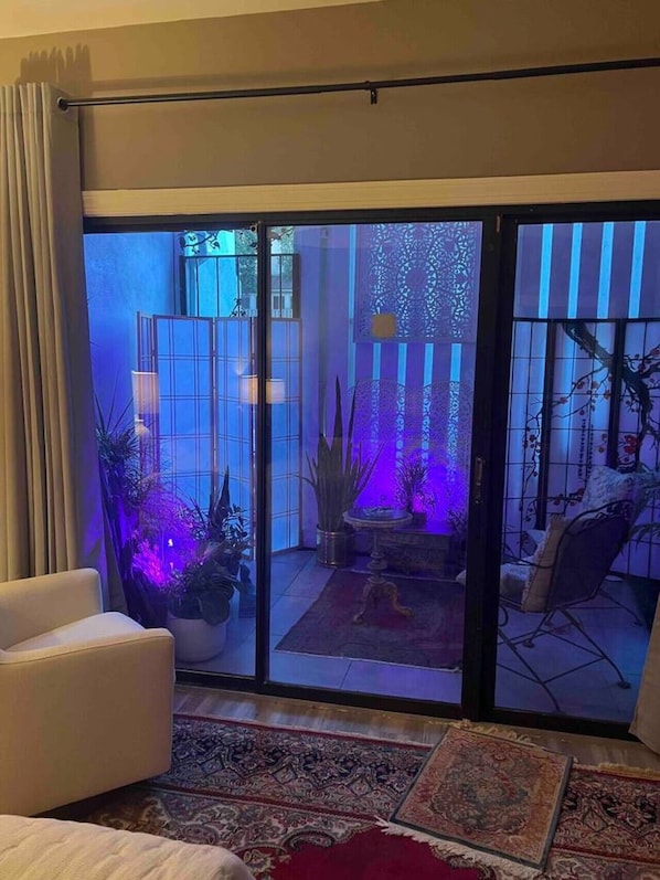 Ein Zimmer mit einer Schiebetür und Zugang zu einer Terrasse mit Pflanzen und einem Stuhl.