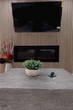 Ein Flachbildfernseher an einer Holzwand, ein Tisch mit einer Topfpflanze und eine Vase mit Blumen.