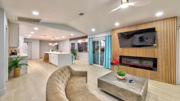Ein modernes Wohnzimmer mit einer gebogenen Couch, einem Holztisch, einem flachbildfernseher an einer Holzwand und einem Deckenventilator.