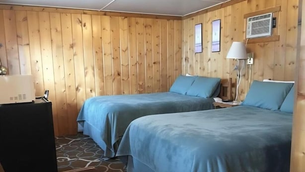 A room with two beds, a desk, a lamp, and a wall-mounted air conditioner. - Hilltop Motel (Montello)