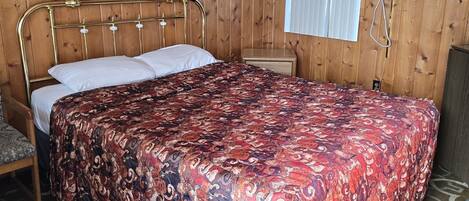 Una cama individual con una colcha estampada en una habitación con paredes de madera y un ventanal con persianas.