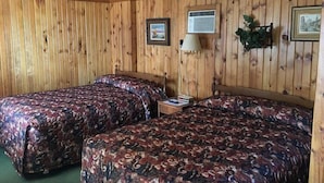 A room with two beds, wooden walls, a ceiling fan, a nightstand with a lamp, and framed pictures. - Hilltop Motel (Montello)