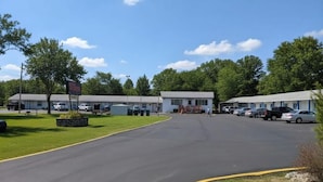 A motel with multiple units, a parking lot, and a clear sky. - Hilltop Motel (Montello)