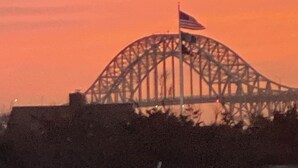A large steel bridge with an American flag, surrounded by trees and a clear sky.
