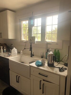 A kitchen with white cabinets, a sink, a window with a view, and various kitchen items on the counter.