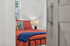 A bedroom with a bed, a window with blinds, a bedside lamp, and a door. - New! Cozy home, Game Room + Covered Porch (Austin)