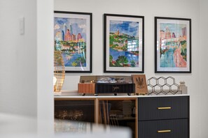 A room with a desk, framed cityscape paintings, and a vintage radio. - New! Cozy home, Game Room + Covered Porch (Austin)