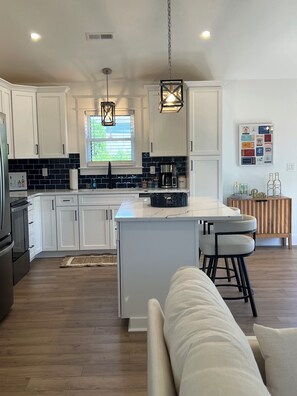 A modern kitchen with white cabinets, a central island, and a bar area. - Water Views and Great Location - BRAND NEW - 3 bedroom 3 bath soundside cottage (Kill Devil Hills)