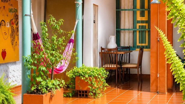 Un patio con mesa, sillas, plantas en macetas, una hamaca y una pared con un mural.